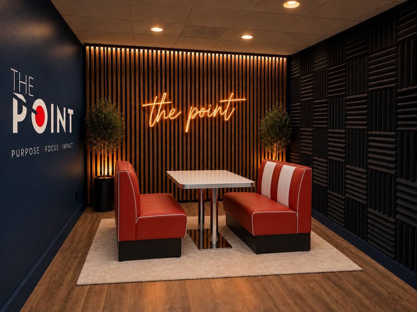 Inside The Point podcast studio in West Columbia: red and white diner booth facing a lit wood slat wall with acoustic foam panels